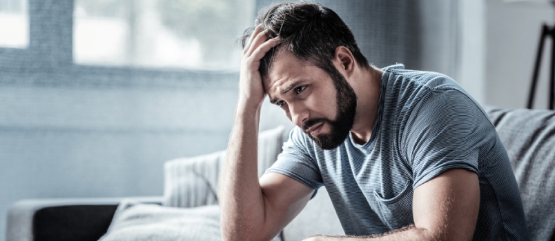 Unpleasant Pain. Sad Unhappy Handsome Man Sitting On The Sofa And Holding His Forehead While Having Headache